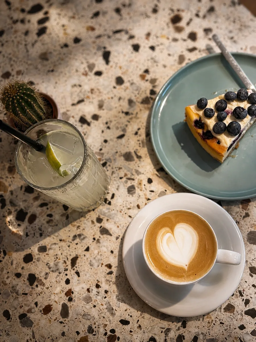 Cappuccino mit Latte-Art, Käsekuchen mit Blaubeeren und Limonade im Cafe de Villa