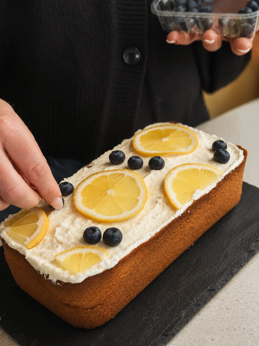 Hausgemachter Rührkuchen mit Sahne, Zitronenscheiben und frischen Heidelbeeren wird dekoriert